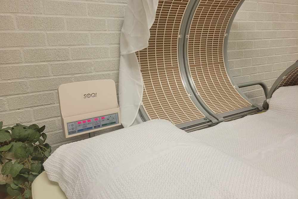 The SOQI Bed HotHouse at Balance & Bloom Wellness: a far-infrared dome beside a linen-covered treatment bed